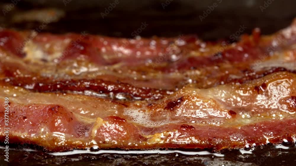 Close-up view of bacon slices in frying pan.