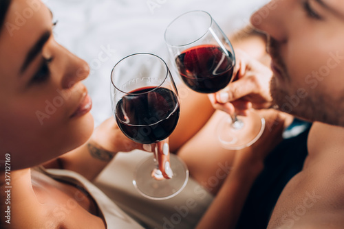 Selective focus of young couple looking at each other while toasting with wine on bed