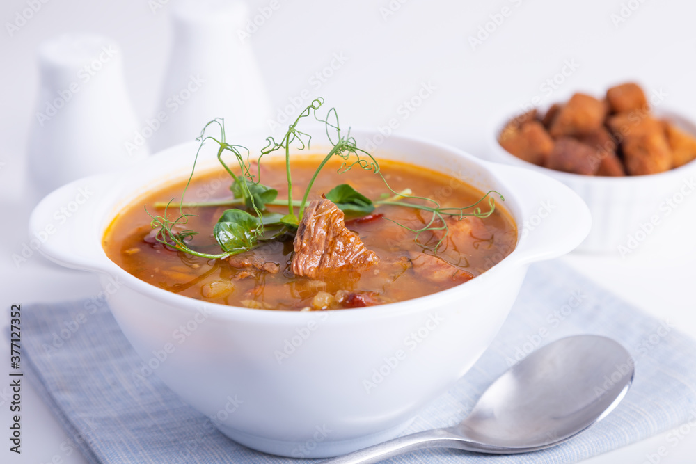 Pea soup with meat, smoked sausage, pea sprouts and croutons. Traditional Russian dish. Home kitchen. Close-up, selective focus. Pea soup with meat, smoked sausage, pea sprouts and croutons. Traditional Russian dish. Home kitchen. Close-up, selective focus.