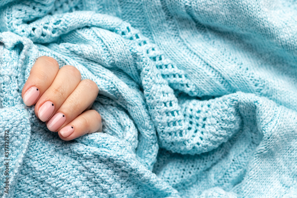 Female hand in a blue knitted sweater fabric with trendy beautiful manicure - pink nude nails with black small dots with copy space. Selective focus Female hand in a blue knitted sweater fabric with trendy beautiful manicure - pink nude nails with black small dots with copy space. Selective focus