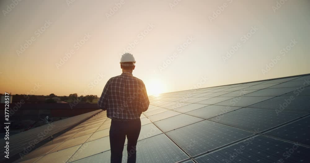 An young engineer is checking with tablet an operation of sun and cleanliness on field of photovoltaic solar panels on a sunset. 