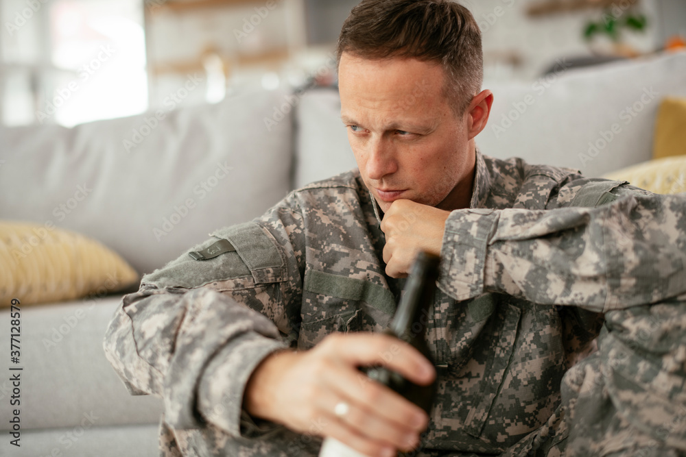 Depressed soldier with bottle sitting in livig room., Alcohol addiction.. Depressed soldier with bottle sitting in livig room., Alcohol addiction..