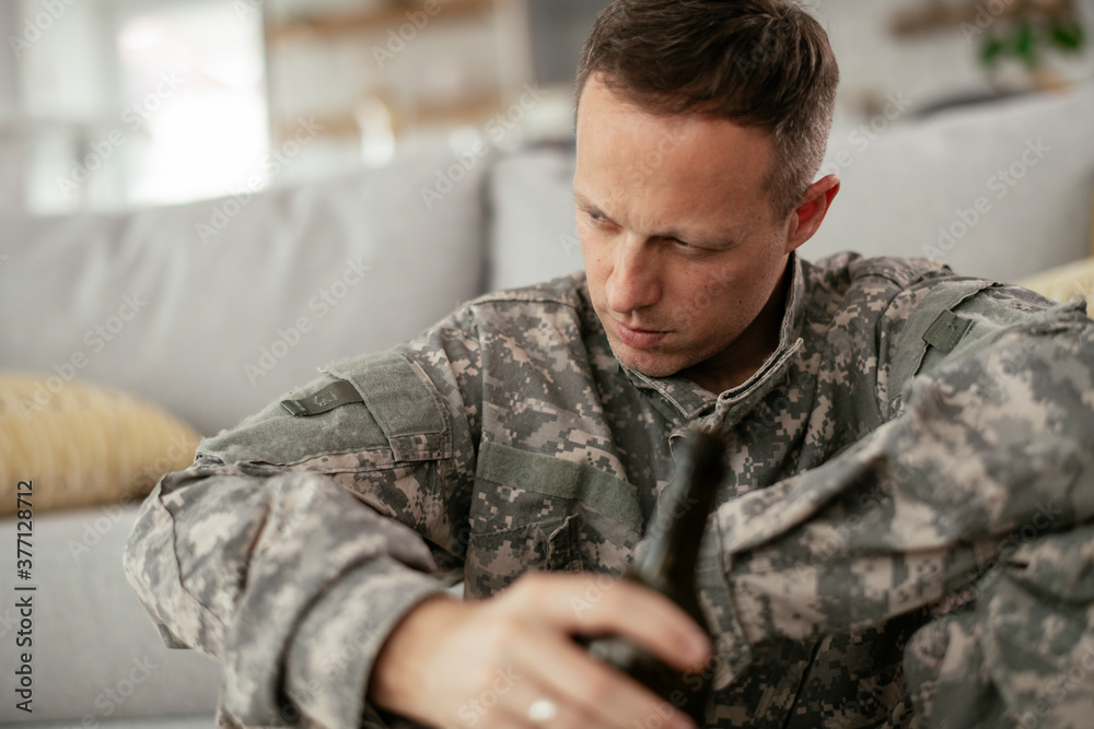 Depressed soldier with bottle sitting in livig room., Alcohol addiction.. Depressed soldier with bottle sitting in livig room., Alcohol addiction..
