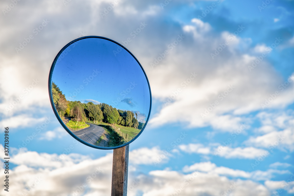 Round mirror on a post in a countryside road. Mirror to help transport. Help cornering. Background of blue sky. Give Way. Round mirror on a post in a countryside road. Mirror to help transport. Help cornering. Background of blue sky. Give Way.