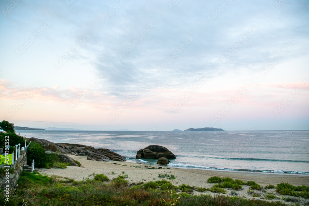 Naklejka premium Photo of the beach in Galicia during sunrise. Beautiful pink and yellow clouds, empty beach. Amazing light during holidays.