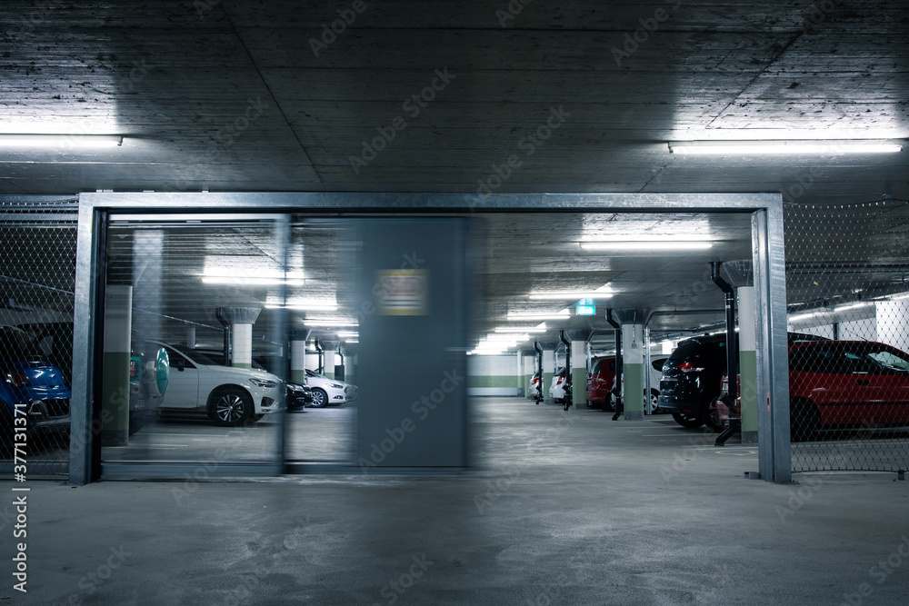 Gated underground parking. Cars parked in a garage with no people. Many cars in parking garage interior. Underground parking with cars (color toned image) Gated underground parking. Cars parked in a garage with no people. Many cars in parking garage interior. Underground parking with cars (color toned image)