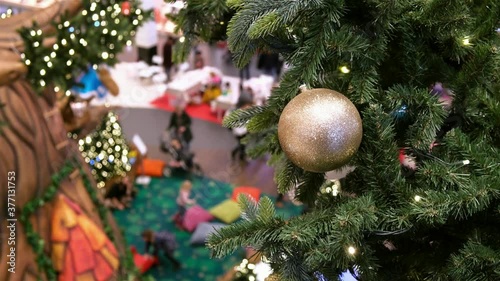 Golden ball and LED garland on artificial Christmas tree in decorated shopping mall. Blurred children playing, people walking on New Year sales. Top view.