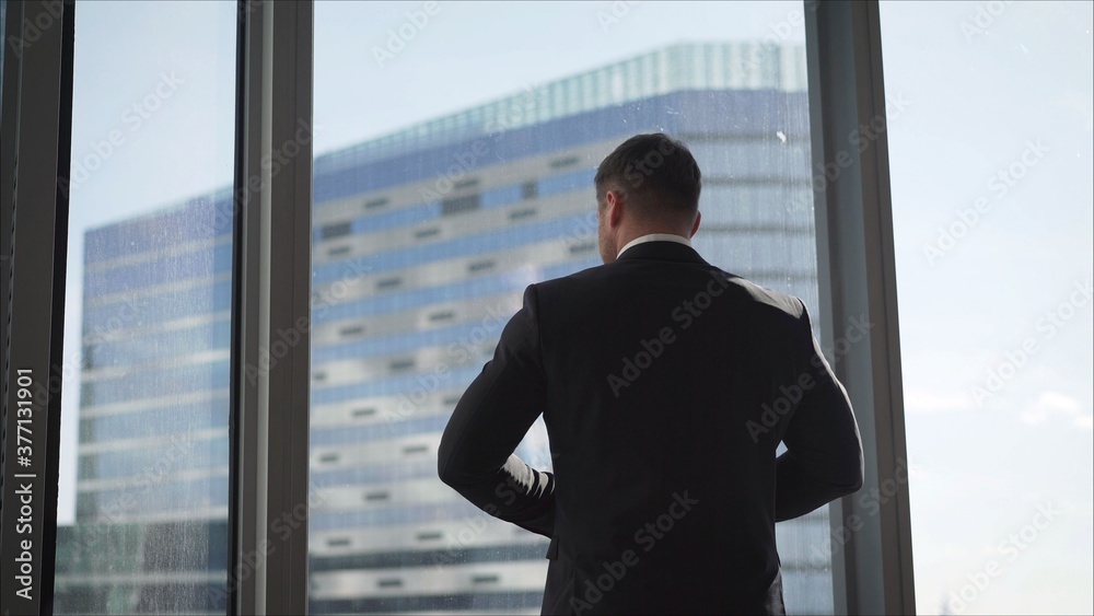 Fototapeta premium Successful businessman in his office. The businessman confidently approaches the window.