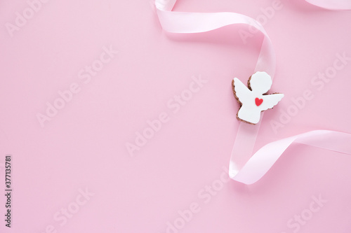 Cookies in the shape of an angel with pink ribbon on pink background.