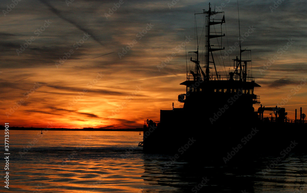 Silhouette image of fishing boat lighted by sunset