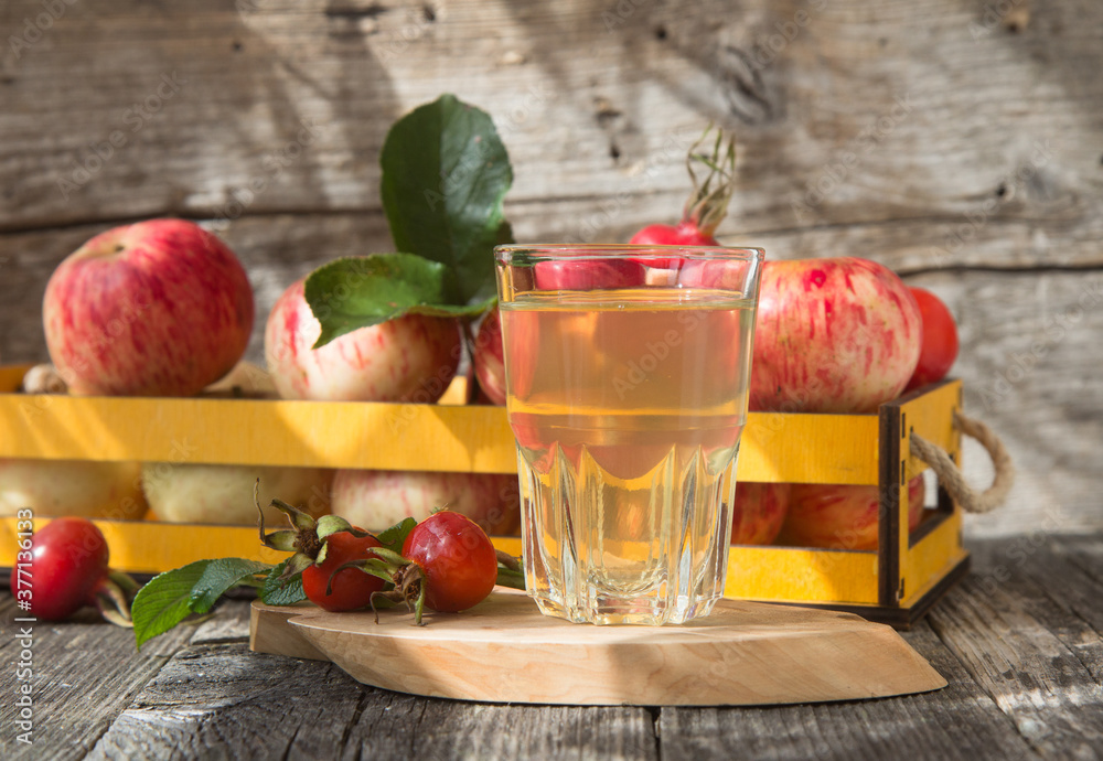 A glass of apple juice and fresh apple on a wooden background in the sunlight. A glass of apple juice and fresh apple on a wooden background in the sunlight.