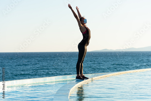 Young woman with protective surgical face mask performing yoga stretching exercises outdoor during covid-19 coronavirus pandemic