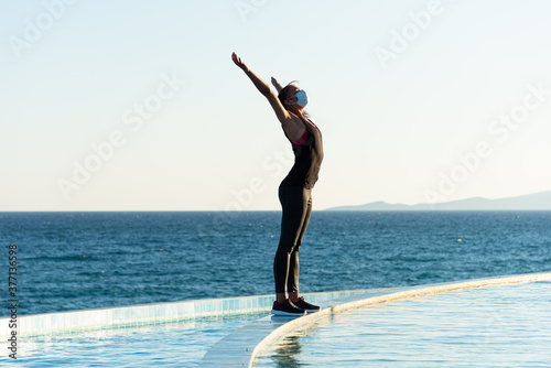 Young woman with protective surgical face mask performing yoga stretching exercises outdoor during covid-19 coronavirus pandemic
