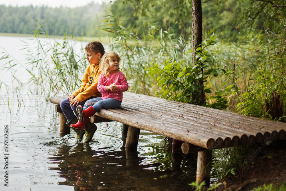 Brother and sister sitting on the river pier. happy children playing together . Boy and girl near lake
