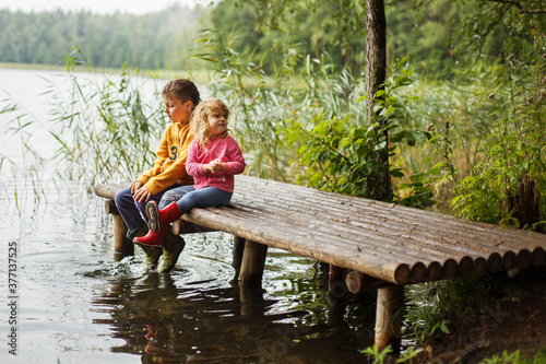 Brother and sister sitting on the river pier. happy children playing together . Boy and girl near lake