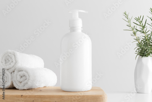 White cosmetic liquid soap dispenser bottle mockup with towels and a rosemary on a wooden table.