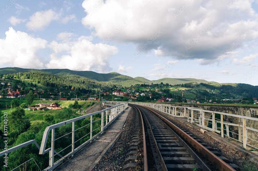Railway track on the bridge on the background of a beautiful mountain landscape. Suburban railway on the background of the village and mountains. Vorokhta. Ukraine, Carpathians