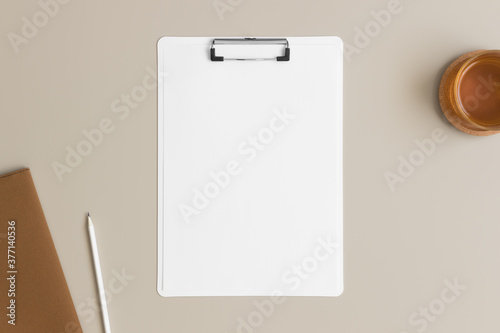White clipboard mockup with a cup of tea and workspace accessories on a beige table.