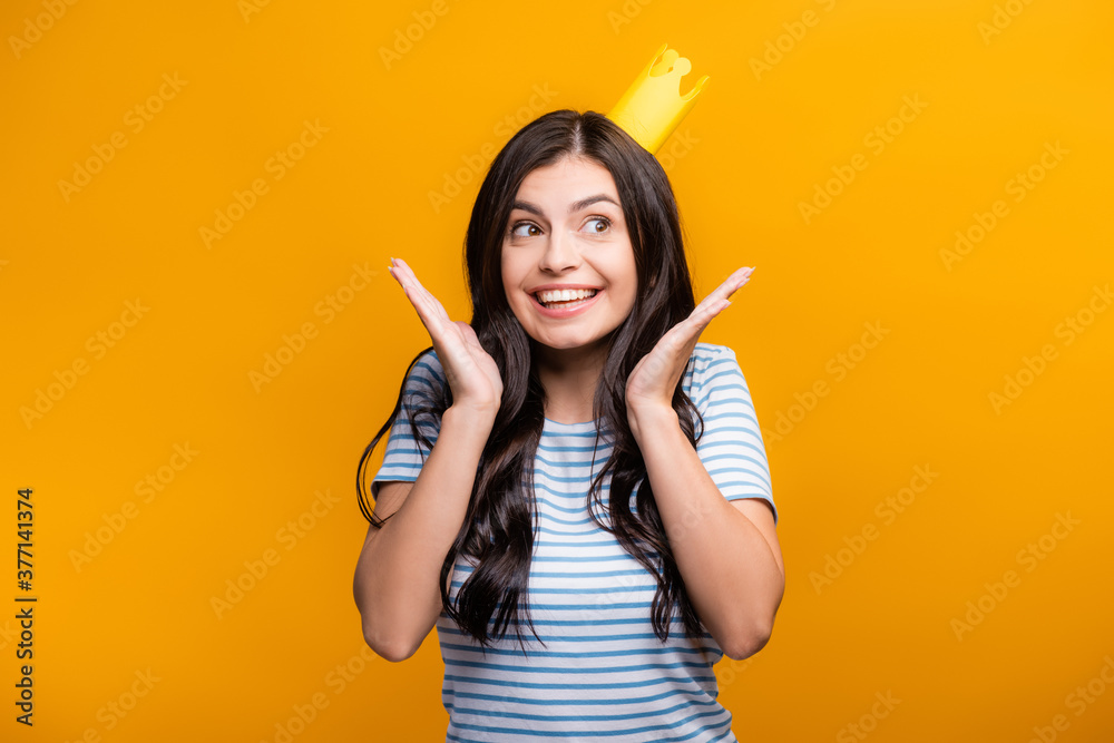 brunette woman in paper crown smiling and looking away isolated on yellow brunette woman in paper crown smiling and looking away isolated on yellow