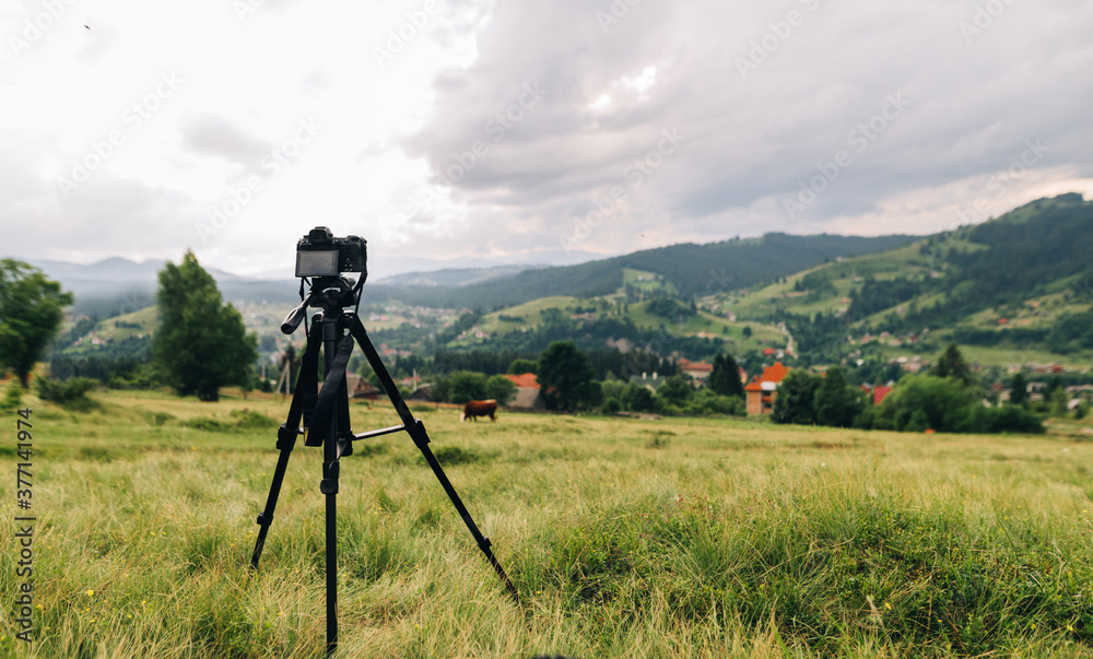 Camera on a tripod captures a beautiful mountain landscape with a village and a forest. Camera on a tripod on the background of a small mountain town. Landscape photography Camera on a tripod captures a beautiful mountain landscape with a village and a forest. Camera on a tripod on the background of a small mountain town. Landscape photography
