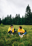 Vertical photo of two happy tourists resting sitting on a meadow in the mountains. Pass on the grass in the mountains in two positive women. Mountain hike
