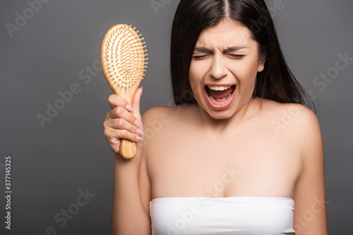 brunette woman holding hairbrush and yelling isolated on black