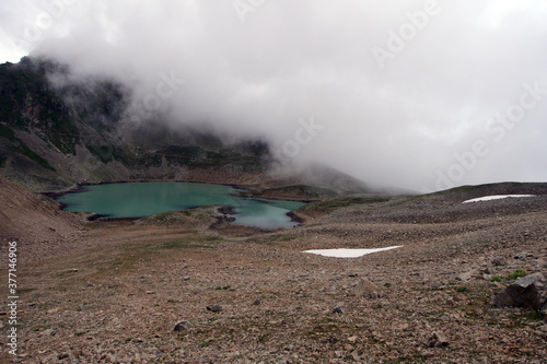 Alpine lake in the clouds. Alpine lake with rocky shores and emerald water in the clouds. Alpine lake Giybashkel (3240 meters above sea level), Caucasus. View from Yakov Pass.