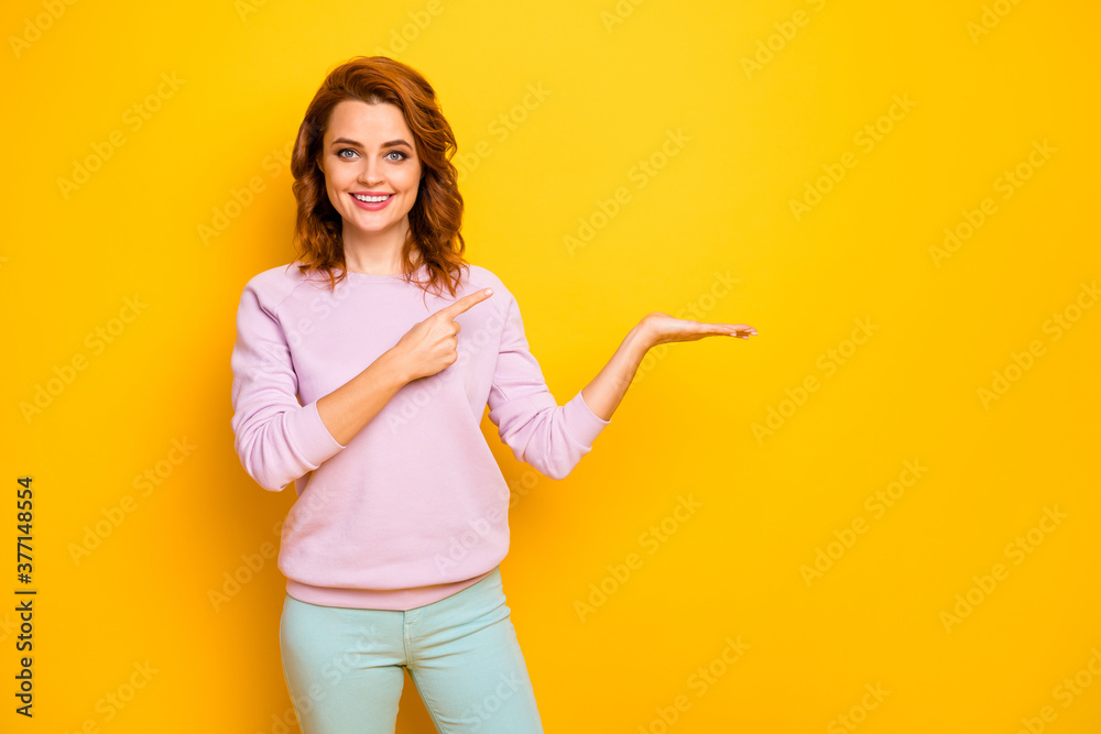 Photo of positive sales manager lady hold novelty indicating finger product on open arm advising low prices shopping wear pink sweater green pants isolated yellow color background Photo of positive sales manager lady hold novelty indicating finger product on open arm advising low prices shopping wear pink sweater green pants isolated yellow color background