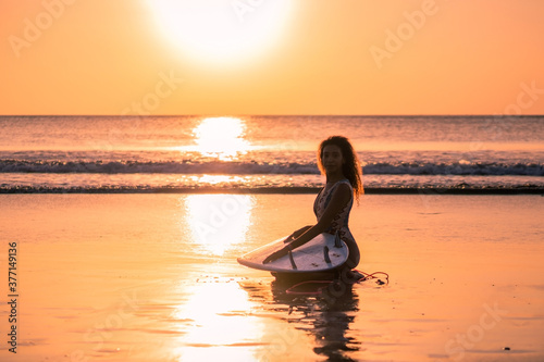 Portrait of woman surfer with beautiful body on the beach with surfboard at colorful sunset. © Lila Koan
