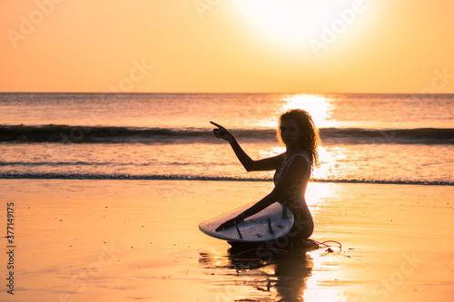 Portrait of woman surfer with beautiful body on the beach with surfboard at colorful sunset © Lila Koan