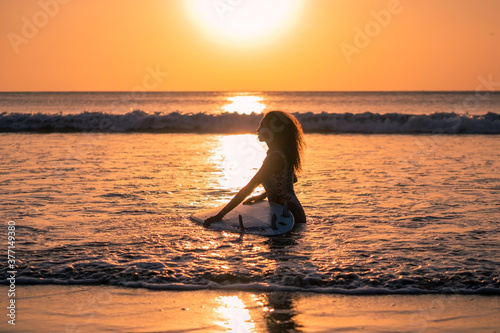 Portrait of woman surfer with beautiful body on the beach with surfboard at colorful sunset © Lila Koan
