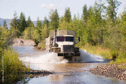 Lorry - a fuel tanker overcomes a water obstacle in a mountainous wooded area. The water level in mountain rivers and streams is constantly changing after rains