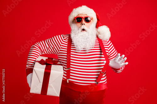 Portrait of his he nice handsome attractive amazed stunned Santa father holding in hands giftbox pulling suspender celebration isolated bright vivid shine vibrant red color background © deagreez