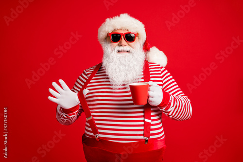 Portrait of his he nice handsome attractive cheerful cheery confident Santa father drinking eggnog pulling suspender having fun isolated bright vivid shine vibrant red color background © deagreez