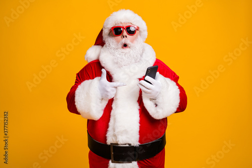 Portrait of his he nice attractive amazed fat overweight bearded Santa demonstrating device gadget web service shopping order delivery isolated bright vivid shine vibrant yellow color background