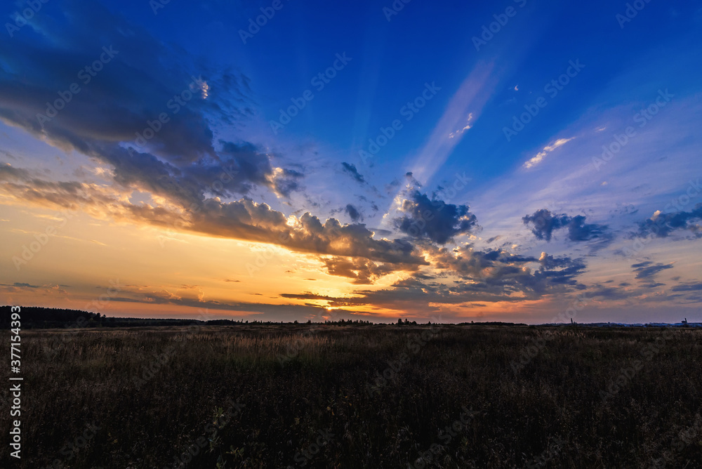orange blue sunset with sun rays through the clouds in the sky in the field in the evening orange blue sunset with sun rays through the clouds in the sky in the field in the evening