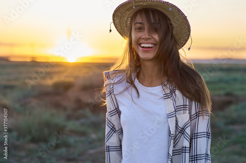 Emotional portrait happy hipster woman on sunset in nature view. Hipster treveler girl in hat in golden sun rays on background. wanderlust travel concept photo