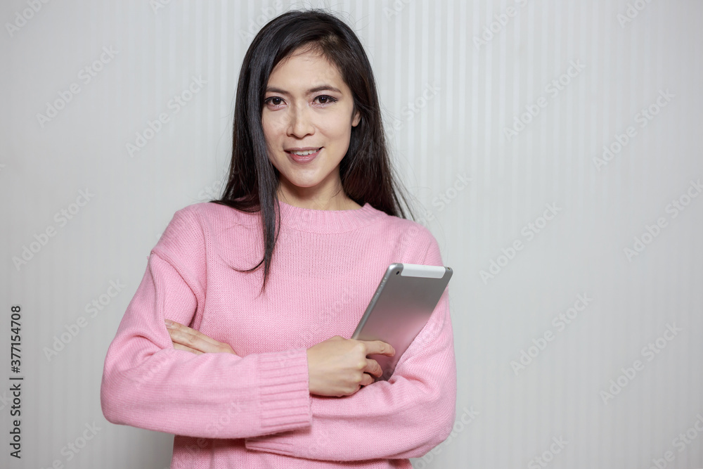 Confident Asian woman smiling and holding a tablet on gray background