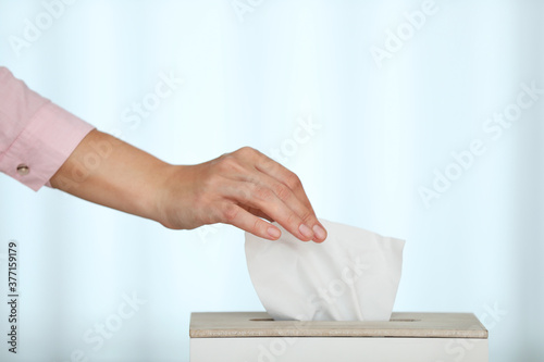 Woman taking paper tissue from holder on light background, closeup
