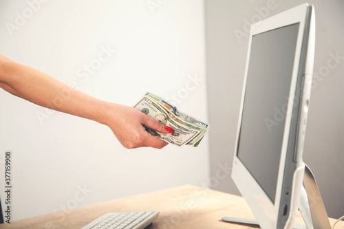 Close-up of hands shopping paying online using laptop while holding US dollars