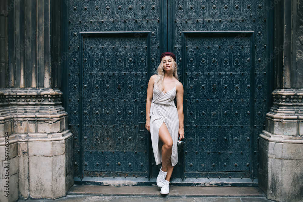Full length portrait of pretty Caucasian fashion model dressed in stylish apparel posing in historic center, trendy hipster girl in gorgeous outfit looking at camera during travel sightseeing Full length portrait of pretty Caucasian fashion model dressed in stylish apparel posing in historic center, trendy hipster girl in gorgeous outfit looking at camera during travel sightseeing