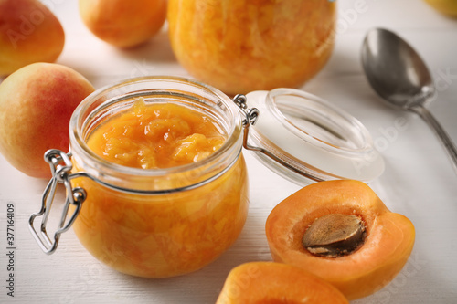 Jar of apricot jam and fresh fruits on white wooden table, closeup