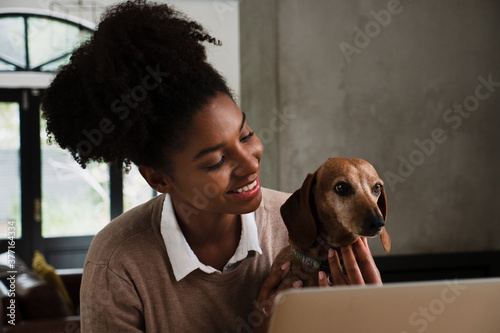 Cute portrait of female teen playing with cute pupping sitting in front on laptop in modern kitchen photo