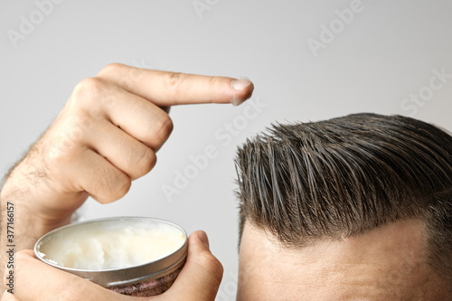 Man applying a clay, pomade, wax, gel or mousse from round metal box for styling his hair after barbershop hair cut. Advertising concept of mans products. Treatment and care against lost of hair photo