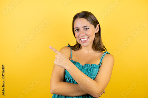 Young beautiful woman over isolated yellow background smiling happy pointing with hand and finger to the side