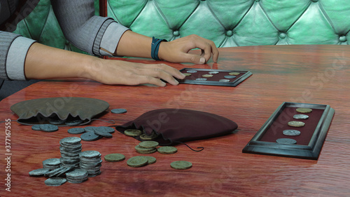 3D render illustration of a man's hand lying freely on the table, which touches a case with ancient coins and wallets lying next to them with spilled Chinese and French coins
