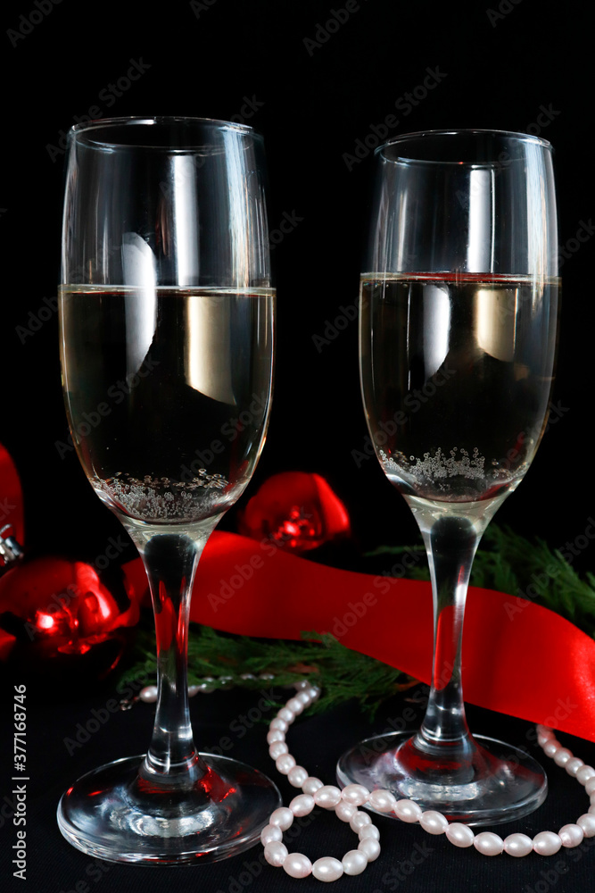 Two glasses of champagne on the festive table on a dark background. next to Christmas decor red balls, ribbon, beads. Christmas composition. Selective focus Two glasses of champagne on the festive table on a dark background. next to Christmas decor red balls, ribbon, beads. Christmas composition. Selective focus