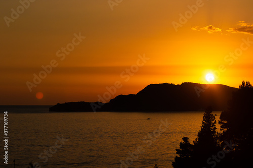 Orange sunset with silhouettes in the sea with mountains, beautiful perfect landscape in the evening by the sea