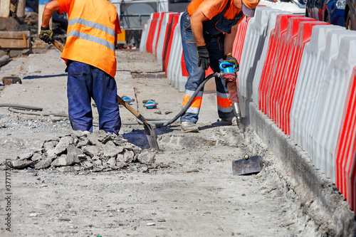 During road repairs, a team of workers cleans old concrete with a jackhammer and shovel.