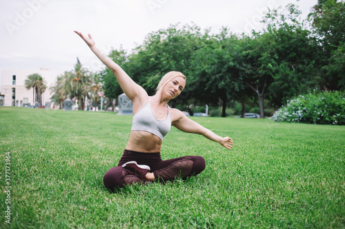 Fit young sportswoman practicing yoga pose on green lawn in park